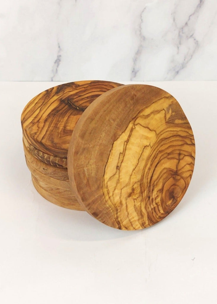 A stack of seven circle olive wood coasters, each featuring unique natural grain patterns