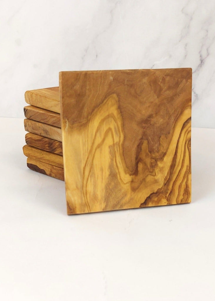 A stack of seven square olive wood coasters, each featuring unique natural grain patterns